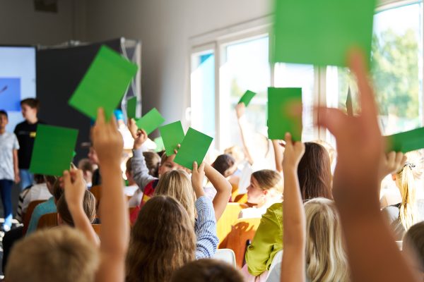 Viele Kinder im DOCK halten grüne Abstimmungskärtchen hoch.